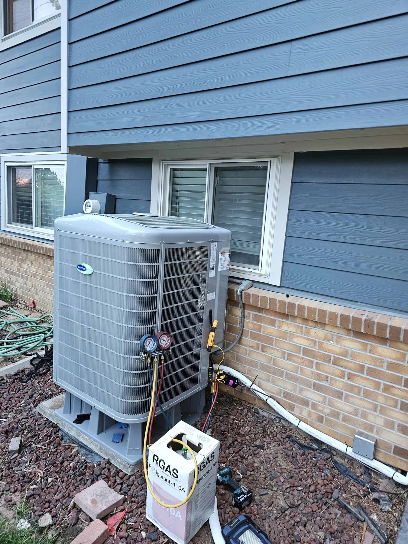 Carrier outdoor unit being tested beside blue siding and a brick wall