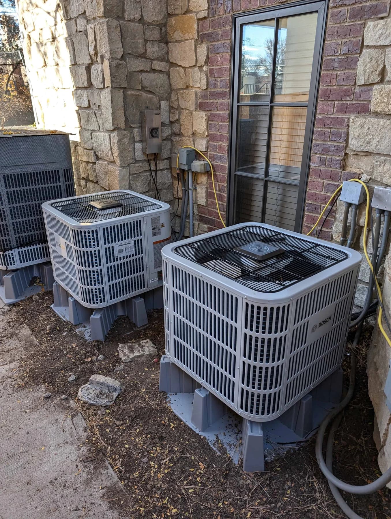 Two Bosch outdoor units installed beside a stone and brick wall