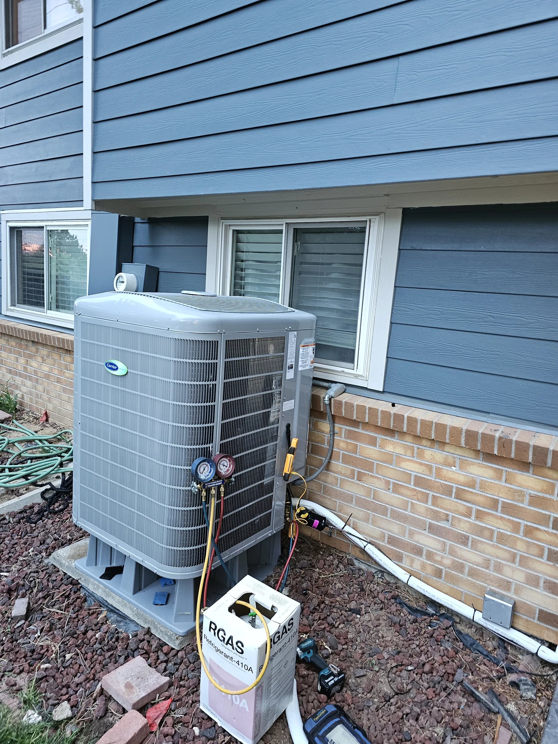 Carrier outdoor unit with refrigerant gauges connected and a jug of refrigerant beside it