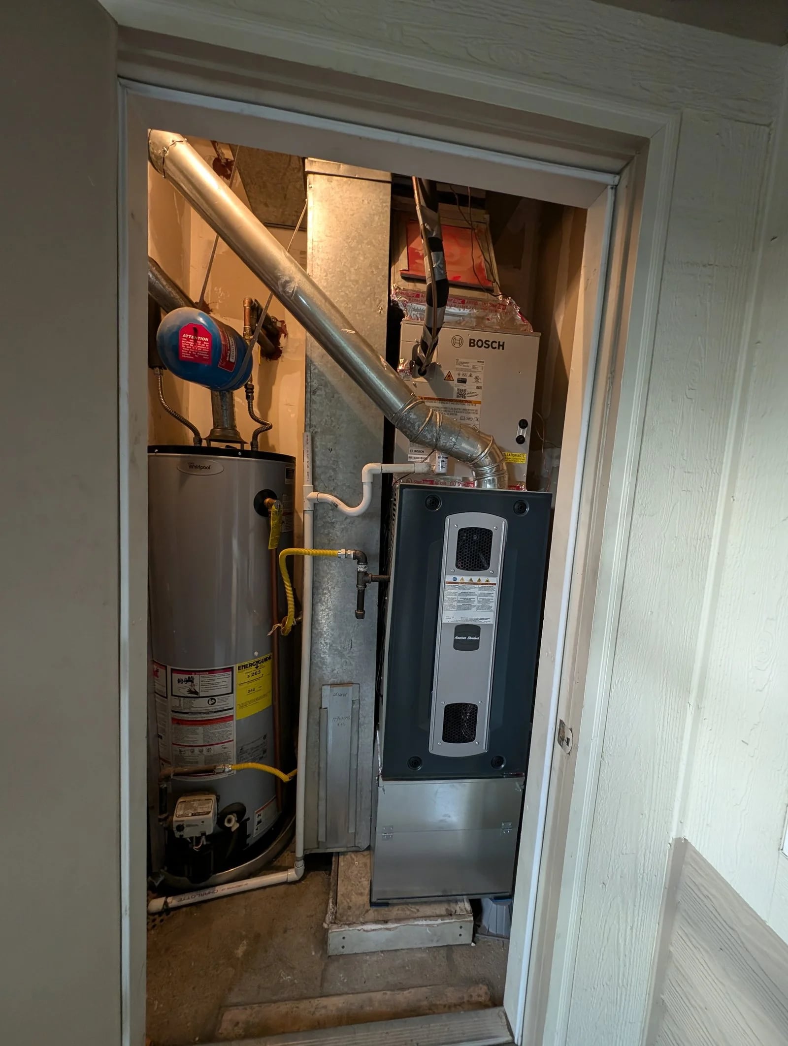 An American Standard furnace under a Bosch coil in a closet beside the water heater
