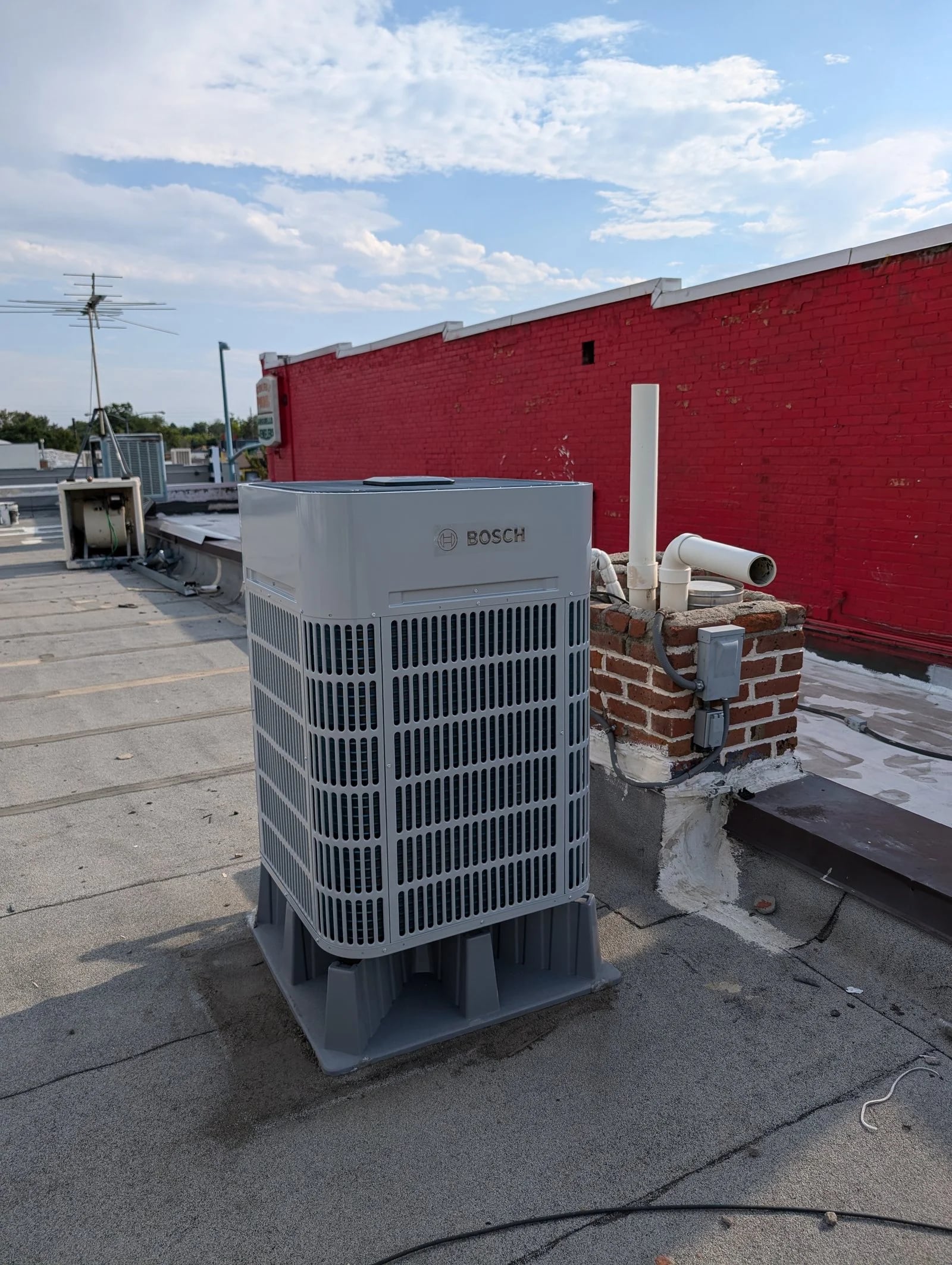 A Bosch outdoor unit on riser feet on a flat roof beside a red parapet wall