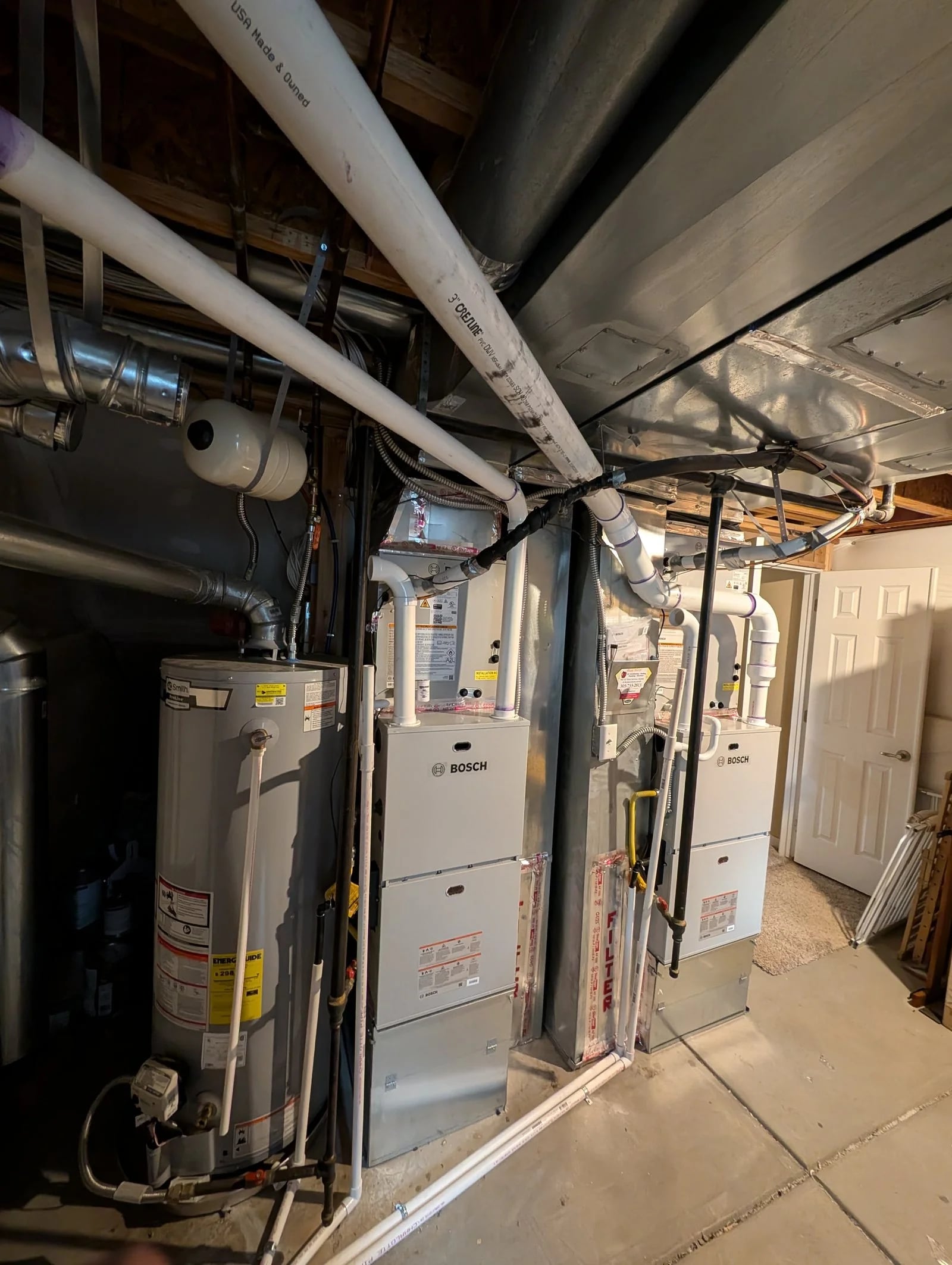 Two Bosch furnaces in an unfinished basement next to the water heater