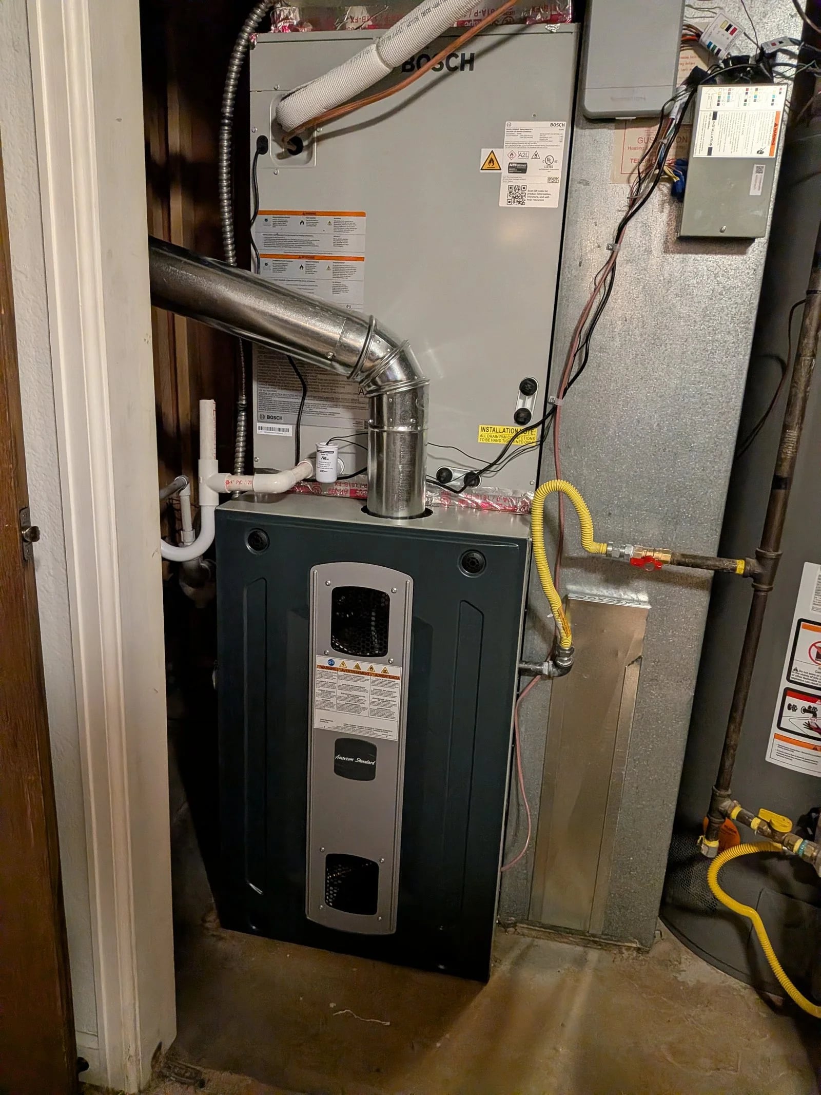 An American Standard furnace with a Bosch coil and white PVC venting in a basement
