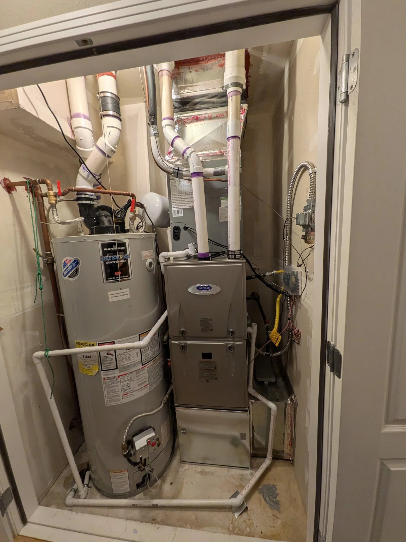 A Carrier furnace beside a Bradford White water heater in a utility closet