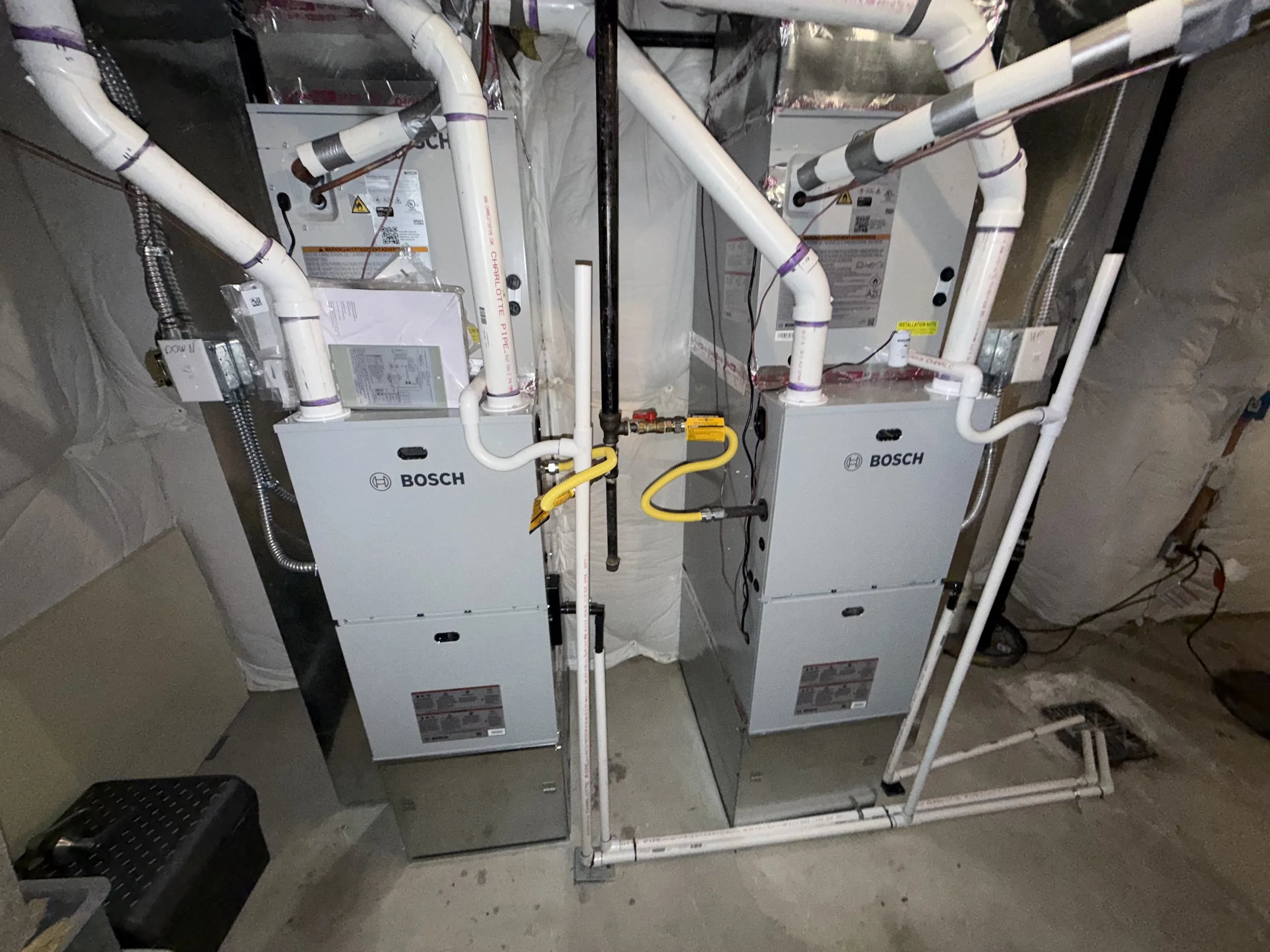Two Bosch gas furnaces side by side in a basement, each with white PVC intake and exhaust